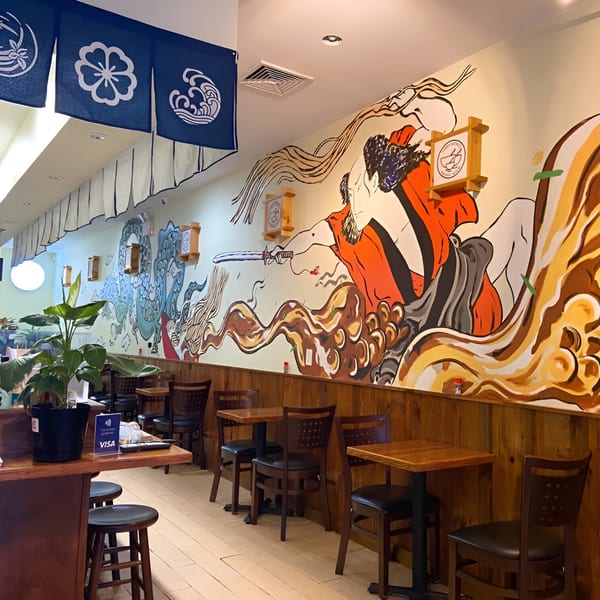 Three Bowls Ramen interior with a large Japanese mural, wooden tables, chairs, and blue decorative banners.
