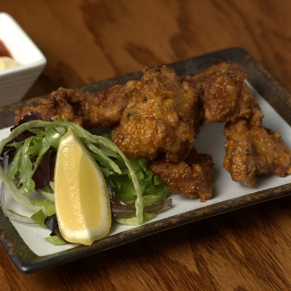 Crispy Japanese fried chicken (karaage) with a lemon wedge and fresh greens on a rectangular plate.