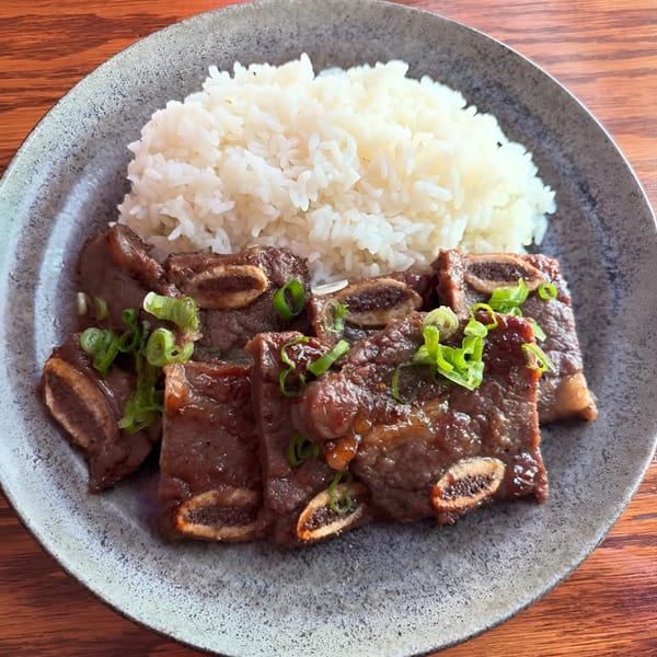 Kalbi short ribs with white rice and green onions on a gray plate.