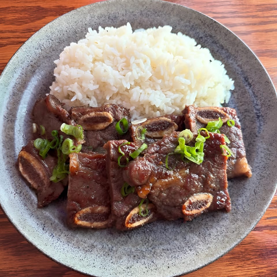 Kalbi short ribs with white rice and green onions on a gray plate.