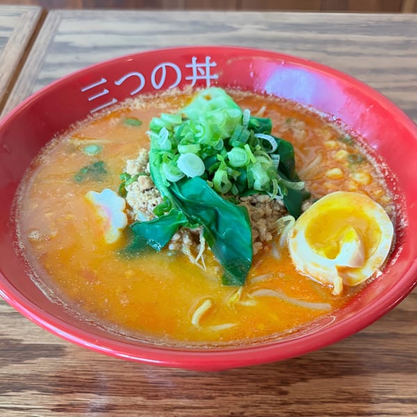 Spicy ramen in a red bowl, topped with ground pork, green onions, and a soft-boiled egg.